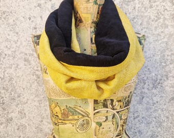 May include: A two-tone infinity scarf in yellow and navy blue. The scarf is draped over a mannequin covered in comic book pages. The yellow portion has a textured, woven appearance.