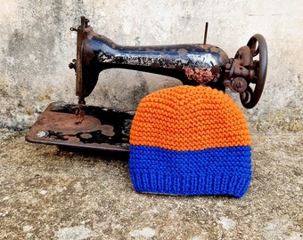 May include: A blue and orange knitted beanie hat sitting on top of an old sewing machine.