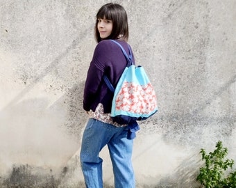 May include: A person wearing a purple sweater and blue jeans is carrying a blue and white drawstring backpack with a floral pattern.