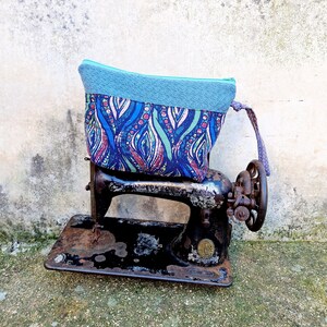 May include: A blue and pink patterned fabric pouch with a light blue fleece lining sits on top of an antique black sewing machine.