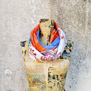 May include: A white, blue and orange patterned scarf is displayed on a vintage mannequin covered in comic book pages. The scarf has a paisley design.