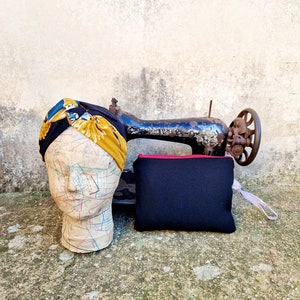 Pode incluir: Uma bolsa de tecido preta com um zíper vermelho e uma alça rosa, uma máquina de costura vintage e uma cabeça de manequim com um turbante estampado em amarelo e azul.
