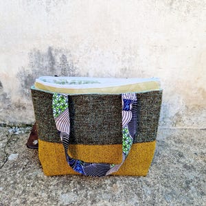 la borsa poggiata davanti la macchina da cucire, con i manici abbassati e la cerniera della pochette interna aperta per far vedere la fodera in cotone