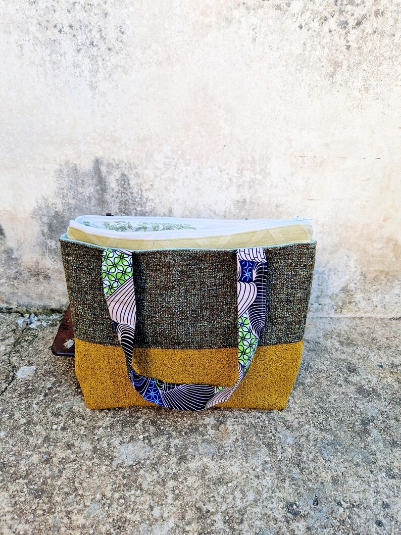 la borsa poggiata davanti la macchina da cucire, con i manici abbassati e la cerniera della pochette interna aperta per far vedere la fodera in cotone