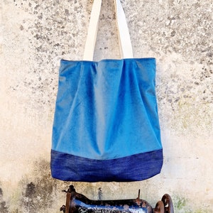 May include: A blue tote bag with a denim bottom and white canvas straps hanging on a wall next to an old sewing machine.
