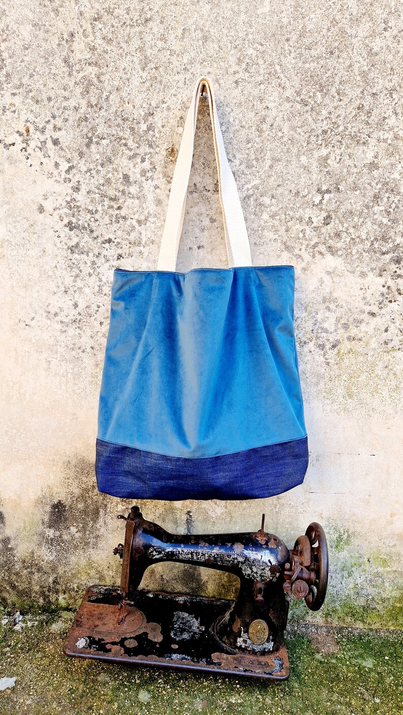 May include: A blue tote bag with a denim bottom and white canvas straps hanging on a wall next to an old sewing machine.