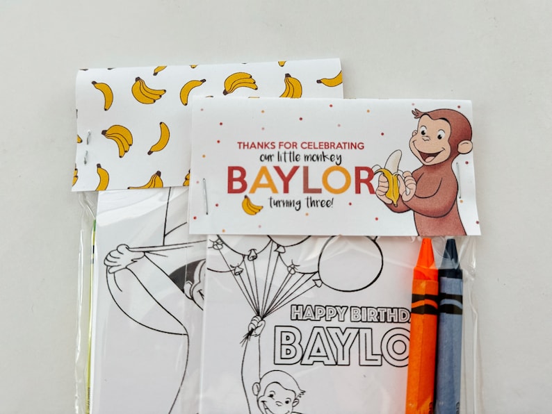 May include: A party favor bag with a Curious George theme. The bag includes a coloring page featuring Curious George holding balloons, a thank you tag that says "Thanks for celebrating our little monkey Baylor turning three!" and two crayons.