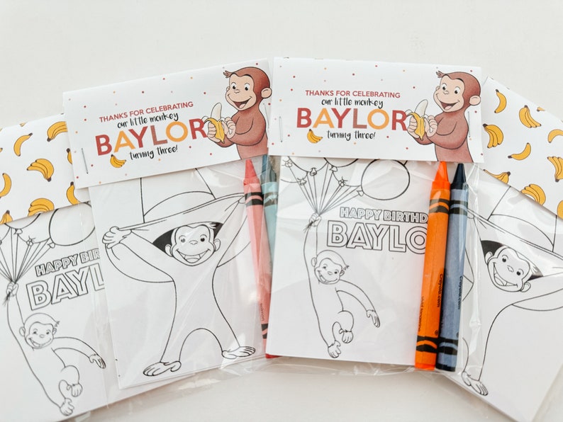 May include: A set of four party favor bags with coloring pages featuring Curious George. Each bag includes a coloring page, two crayons, and a tag that says "Thanks for celebrating our little monkey Baylor turning three!"