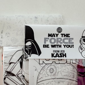 May include: A Star Wars themed coloring page with Darth Vader, a Stormtrooper, and the Death Star. The page is packaged with crayons and a tag that reads "May the Force be with you! From Jedi Kash".