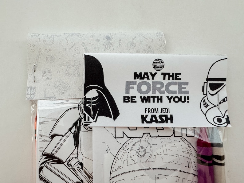 May include: A Star Wars themed coloring page with Darth Vader, a Stormtrooper, and the Death Star. The page is packaged with crayons and a tag that reads "May the Force be with you! From Jedi Kash".