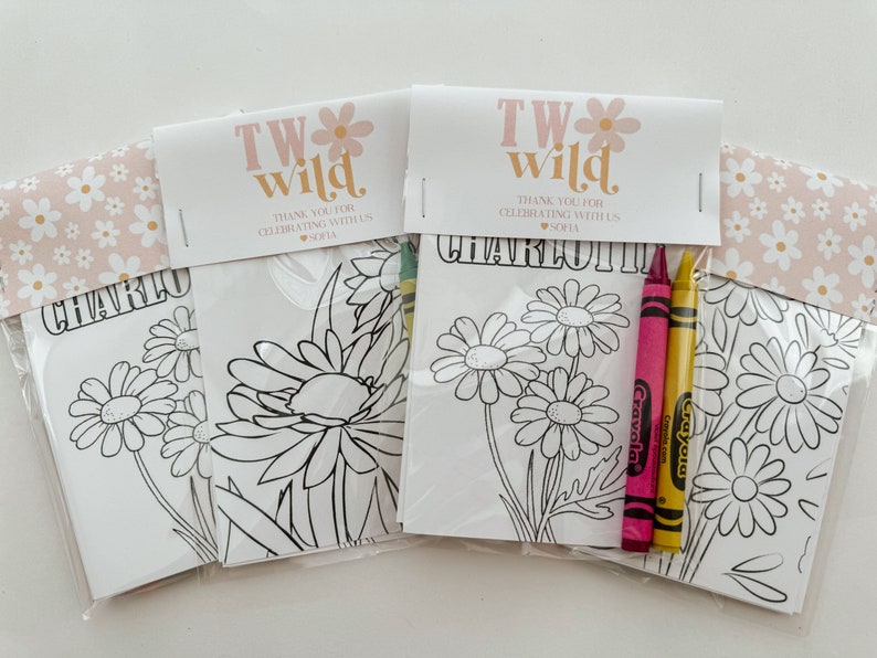 May include: Three white coloring pages with a floral design and the text "TW wild" and "CHARLOTTE" on the top. The pages are packaged in clear plastic bags with two yellow and pink crayons.
