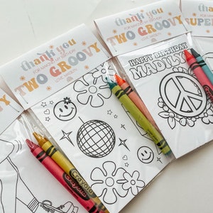 May include: A set of four groovy themed colouring pages with crayons. The colouring pages feature a peace sign, a van, a disco ball, and a girl in a groovy outfit. The text on the pages says "Happy Birthday Madily" and "Thank you for making my birthday two groovy".