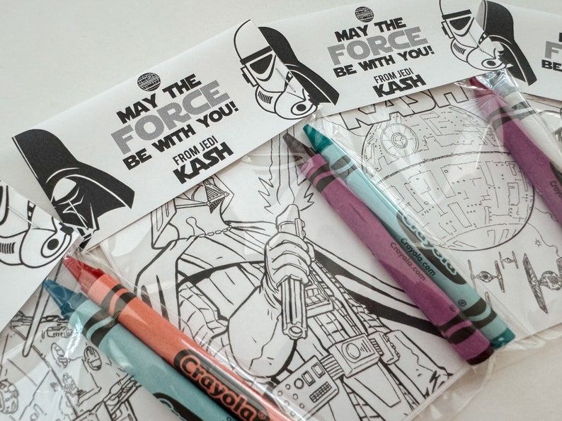 May include: A set of Star Wars themed coloring pages with crayons. The pages feature Darth Vader, a Death Star, and a Stormtrooper. The text on the pages reads "May the Force be with you! From Jedi Kash."