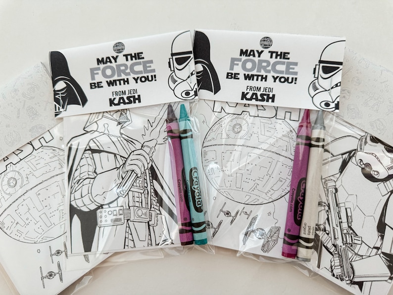 May include: Two Star Wars themed coloring pages with crayons. One page features Darth Vader and the other features the Death Star. The pages have the text "May the Force be with you! From Jedi Kash" on them.