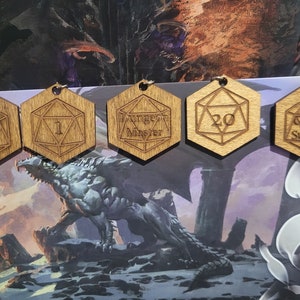 Puede incluir: Cinco dijes hexagonales de madera en forma de dados con diseños grabados. Los dijes representan un dragón, los números 1 y 20, las palabras "Éxito crítico" y "Dungeon Master".