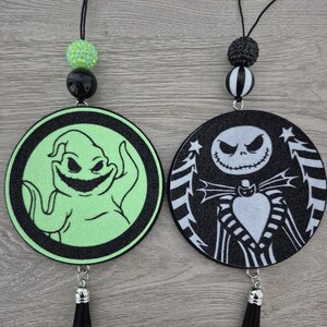 May include: Two circular hanging ornaments featuring characters from The Nightmare Before Christmas. One ornament displays a green Oogie Boogie on a black background, while the other shows a white Jack Skellington on a black background with black tassels.