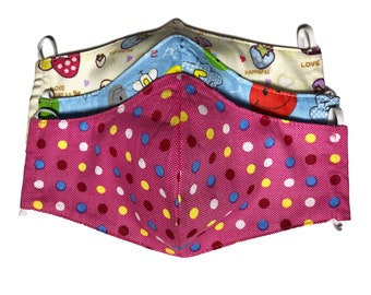 May include: Three reusable face masks with colorful patterns. The top mask is cream with a pink strawberry, a blue elephant, and the words "Love Happiness". The middle mask is blue with a yellow smiley face and the words "Happiness". The bottom mask is pink with white, yellow, blue, and red polka dots.