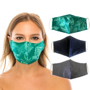 May include: A woman wearing a teal face mask with a white leaf pattern. Three additional face masks are displayed: a teal leaf print, a navy blue mask, and a black and white checkered mask. All masks have white elastic ear loops.