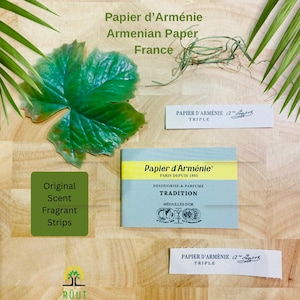Peut inclure: Vue aérienne des produits Papier d'Arménie. L'image présente une feuille verte, un paquet de bandes parfumées Tradition et deux bandes de papier parfumé Triple. Le texte sur l'emballage indique "Papier d'Arménie, Paris Depuis 1885".