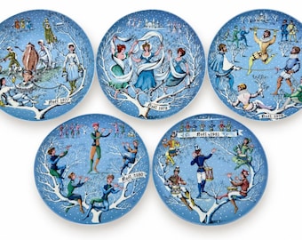 May include: A set of five round blue porcelain collector plates featuring winter scenes with figures in historical attire. Each plate is labeled with the year Noël 1977, 1978, 1979, 1980, or 1981, depicting various activities like dancing, playing instruments, and farming.