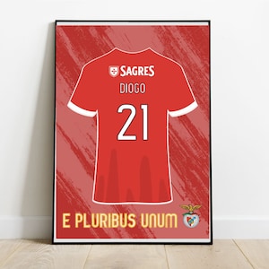 May include: A red and white football shirt with the number 21 on the back. The shirt has the words "SAGRES" and "DIOGO" on the front, along with a crest. The shirt is on a red background with a white border. The words "E PLURIBUS UNUM" are at the bottom of the image.