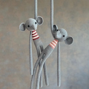 May include: Two grey crocheted monkey toys hanging from a string. Each monkey has a red and white striped shirt and black eyes.