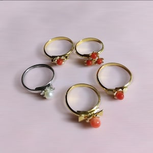 Peut inclure: Cinq bagues en or avec des accents de corail et de perle. Les bagues sont dispos&eacute;es sur une surface rose.