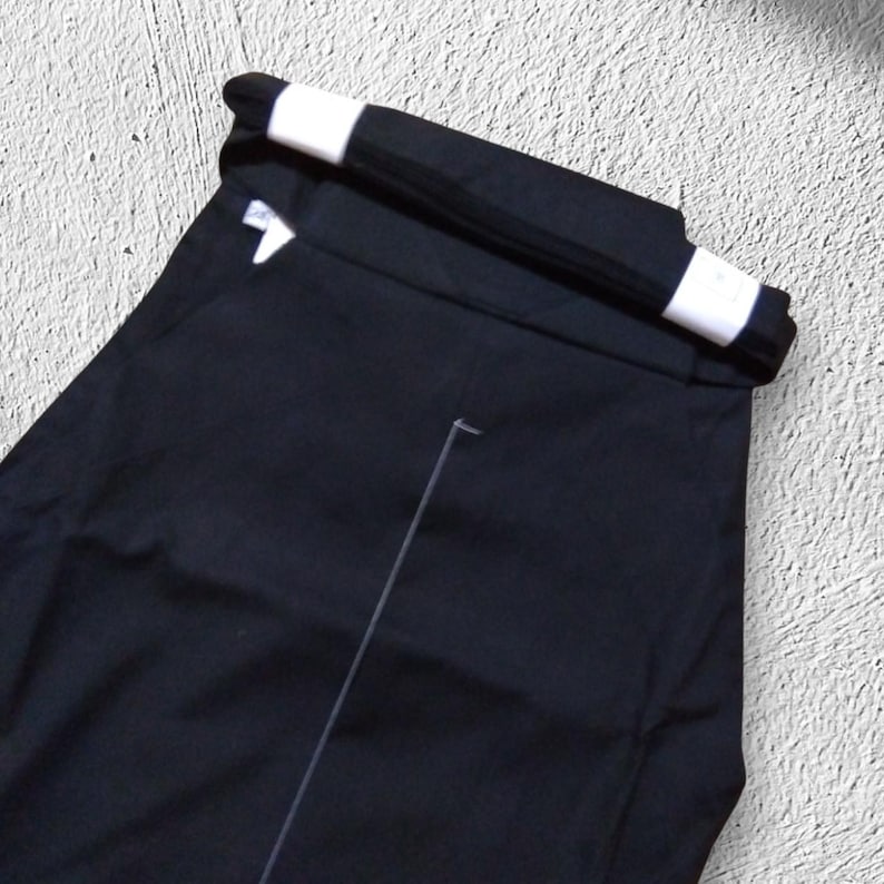 May include: Black pants with a folded waistband featuring white accents. The pants are made of a smooth, dark fabric and appear to be neatly pressed. A white seam line is visible on the front of the pants.