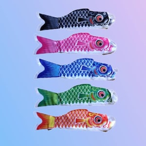 以下が含まれることがあります： 5匹のカラフルな魚の風船が並んでいます。風船は黒、ピンク、青、緑、オレンジです。それぞれの風船は白い背景に黒い輪郭と黒、白、赤の顔があります。