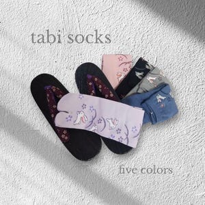 May include: A selection of tabi socks in five colours, designed with a split toe, are shown with traditional Japanese sandals. The socks have a repeating pattern of rabbits and floral accents. The text "tabi socks" and "five colors" are visible.
