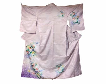 May include: A light pink kimono with floral embroidery. The kimono features a delicate pattern of colorful flowers and foliage on the sleeves and lower portion. The garment is made of a smooth, flowing fabric.