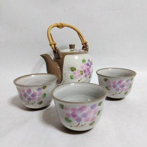 May include: A brown and white ceramic teapot with a bamboo handle and floral design. The teapot is accompanied by three matching teacups with floral designs.