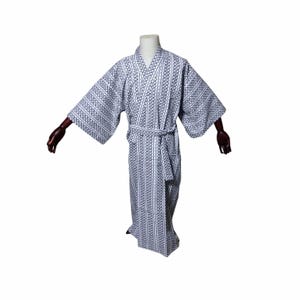 May include: A white and navy blue patterned kimono robe. The robe features a repeating geometric design and a matching belt. The robe is displayed on a mannequin with wooden arms.