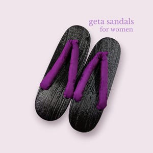 Könnte beinhalten: Ein Paar traditionelle japanische Geta-Sandalen für Frauen. Die schwarzen Holzsohlen haben eine strukturierte Oberfläche, und die Riemen sind leuchtend lila. Der Text "geta sandals for women" wird oben rechts angezeigt.