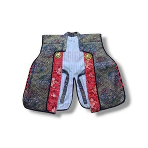 May include: A sleeveless vest featuring a dark fabric with a gold and blue circular dragon pattern, accented by red panels with white dragon motifs. The garment includes two gold-toned circular buttons and a white interior lining with thin stripes.