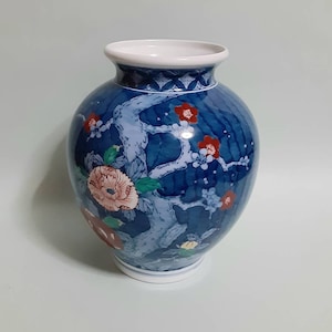 May include: A blue and white ceramic vase with a floral design. The vase has a round body and a narrow neck. The floral design features pink, red, and yellow flowers.