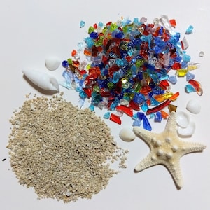 以下が含まれることがあります： ビーチをテーマにした要素の俯瞰図。カラフルな砕いたガラスの山、砂の山、貝殻、白いヒトデがあります。ガラス片は赤、青、緑、黄色です。