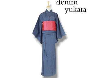 May include: A blue denim yukata featuring wide sleeves and a vibrant red obi sash tied around the waist. The garment is displayed on a mannequin and includes the text denim yukata in the upper right corner of the image.