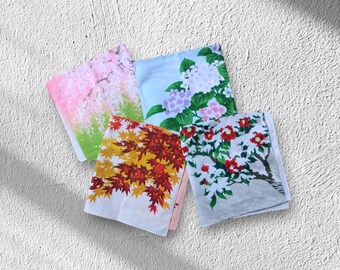 Op de afbeelding: Vier vierkante zakdoeken met bloemmotieven. Eén heeft roze kersenbloesems, een ander paarse en witte hortensia's, een derde rode en gele herfstbladeren en de laatste rode bloemen op een boom.