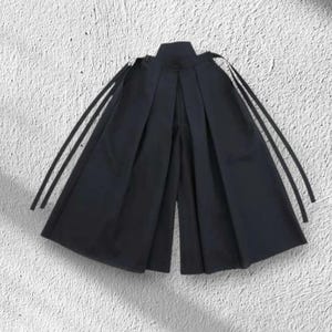 May include: Black culottes with a high waist and wide legs. The pants have a pleated design and long, thin straps attached at the shoulders. The fabric appears to be a smooth, solid color.