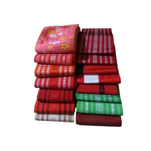 Puede incluir: Una pila de textiles coloridos, con una variedad de patrones y colores. Los textiles incluyen tonos de rojo, rosa y verde, con diseños y rayas intrincados. Las telas están cuidadosamente dobladas y apiladas, mostrando los diversos patrones.