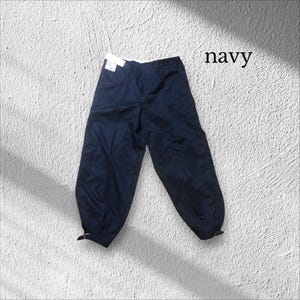 May include: Navy blue trousers with a button and zip fastening. The trousers have a relaxed fit and are gathered at the ankles with adjustable straps. The word "navy" is printed in the upper right corner.