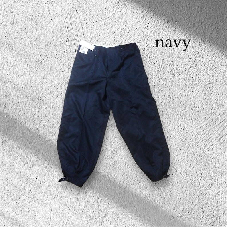 May include: Navy blue trousers with a button and zip fastening. The trousers have a relaxed fit and are gathered at the ankles with adjustable straps. The word "navy" is printed in the upper right corner.