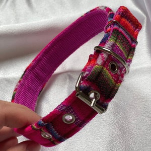 May include: A pink dog collar with a colorful woven pattern and a silver buckle. The collar has two silver eyelets.