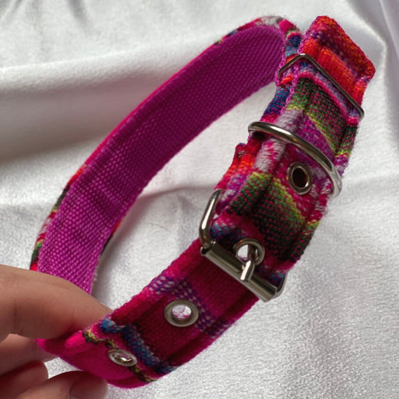 May include: A pink dog collar with a colorful woven pattern and a silver buckle. The collar has two silver eyelets.