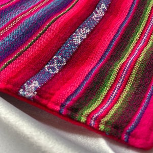 May include: Close-up of a colorful striped fabric with pink, blue, green, and white stripes. The fabric has a woven texture and is made of a soft material.