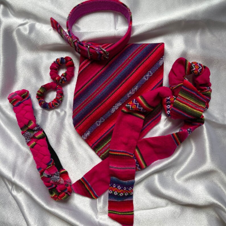 May include: A set of pink and purple patterned fabric accessories, including a headband, a bandana, and two scrunchies. The bandana has a striped pattern with a geometric design.