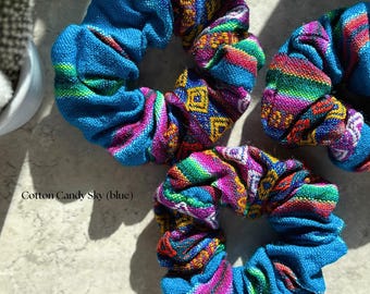 May include: Three colorful hair scrunchies with a blue base and a multi-colored woven pattern. The scrunchies are made of fabric and are perfect for holding hair in place.