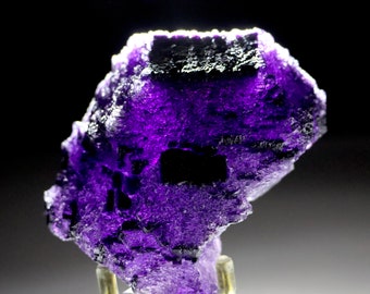 May include: A deep purple fluorite crystal with a rough, textured surface. The crystal is on a display stand.