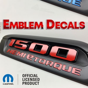 May include: A black 1500 Hemi Torque emblem with red and blue lettering. The emblem is shown in three different styles: OEM, with red lettering, and with red and blue lettering. The image also includes the text "OEM LOOK", "Options below with our decals to change the look", "EMBLEM DECALS", and "OFFICIAL LICENSED PRODUCT".